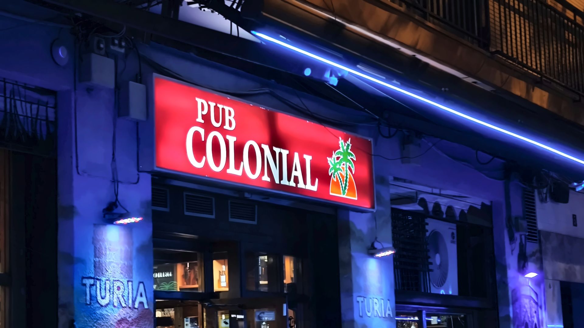Fachada del Pub Colonial de noche, con el rótulo rojo y el neón azul